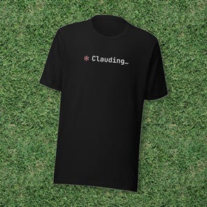May include: A black short-sleeved t-shirt featuring a small pink asterisk symbol followed by the white text "Clauding..." printed on the upper chest area. The garment has a standard crew neckline and a straight hemline design.