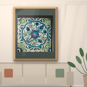 May include: A square ceramic tile featuring a central circular medallion filled with blue and turquoise floral motifs, including tulips and carnations, surrounded by a green and white leafy border, all encased in a light wood frame with a dark mat.