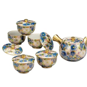 Könnte beinhalten: Keramik-Teeservice mit blauem, gelbem und weißem Blumenmuster. Das Set umfasst eine Teekanne mit goldenem Griff und Ausguss sowie mehrere Tassen mit Deckeln und goldenen Knöpfen.