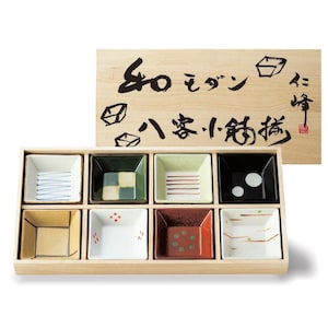 May include: A wooden box set containing eight small, square ceramic dishes. Each dish features a unique design with colors like white, green, black, and red. The wooden lid has Japanese calligraphy.