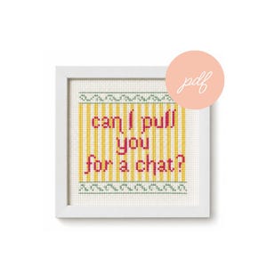 May include: A square white frame containing a cross-stitch pattern on white fabric. The design features vertical yellow stripes and a green geometric border. The text "can I pull you for a chat?" is stitched in pink letters in the center.