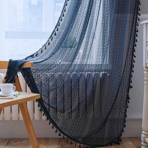 Könnte beinhalten: Ein dunkelblauer, halbtransparenter Vorhang mit vertikalen Streifen aus komplizierten Spitzenmustern und geometrischen Ausschnitten. Die Kanten des Stoffes sind mit kleinen, herabhängenden Quasten verziert, die entlang des Vorhangs verlaufen.