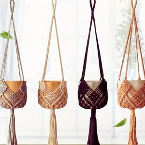 May include: Four macrame plant hangers in beige, tan, and dark brown. Each has a woven design around a cylindrical pot holder and a long tassel. The hangers are suspended from a loop at the top. Ideal for indoor plants.
