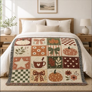 Può includere: Una coperta tessuta con un motivo a griglia di illustrazioni a tema autunnale che include zucche, fiocchi, foglie, fiori, una stella, un motivo a scacchi e una tazza di cioccolata calda nei toni del crema, arancione, marrone e verde bosco.