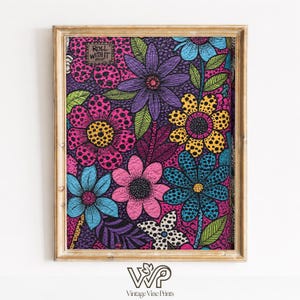 May include: A framed floral print with a gold-coloured frame. The artwork features a vibrant, colourful design of stylised flowers in shades of pink, purple, blue, and yellow, set against a dark background. The text "ROLL WITH IT" is visible.