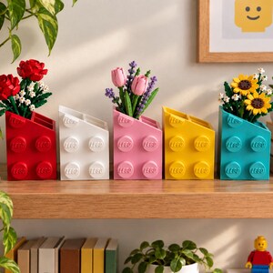 May include: Five rectangular desk organisers shaped like large LEGO bricks in red, white, pink, yellow, and teal. Each organiser features four circular studs embossed with the LEGO logo and holds a different arrangement of colourful brick-built flowers.