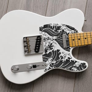 May include: White electric guitar featuring a black and white wave pattern on the body. It has a maple neck and fretboard, chrome hardware, and a single-coil pickup. The guitar is a Telecaster style.