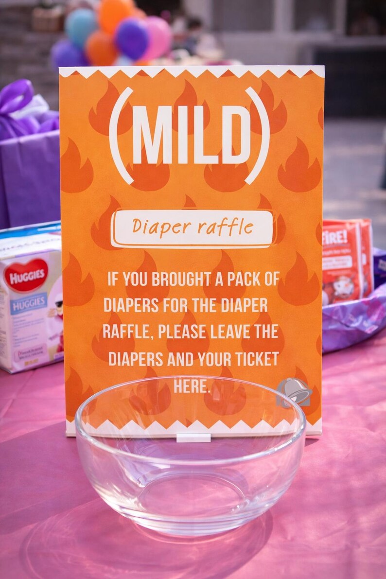 May include: An orange sign with the word "MILD" and "Diaper raffle" printed on it. The sign has a flame pattern and instructions for a diaper raffle. A clear glass bowl sits in front of the sign.
