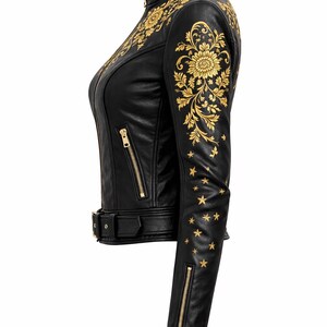 May include: Black leather jacket with gold floral and star embroidery. The jacket has a high collar, a zip front, and a waist belt. The sleeves feature gold zips and star details. A stylish and detailed outerwear piece.