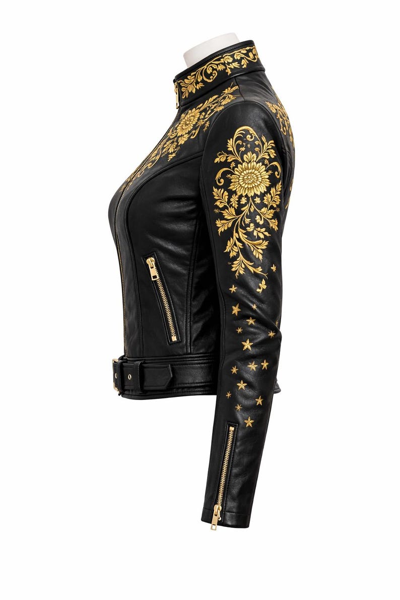 May include: Black leather jacket with gold floral and star embroidery. The jacket has a high collar, a zip front, and a waist belt. The sleeves feature gold zips and star details. A stylish and detailed outerwear piece.