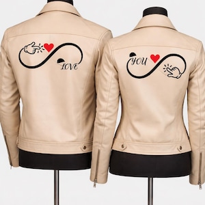 May include: Two beige leather jackets on display. Each jacket has a black infinity symbol with a red heart and a hand gesture. One jacket says "LOVE", the other says "you".