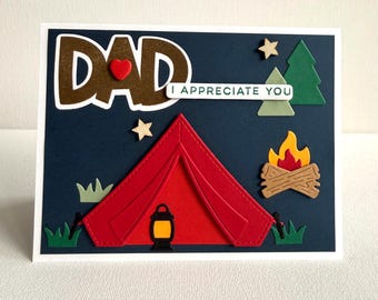 May include: A handmade card with a camping theme. The card features a red tent, campfire, and the words "DAD I APPRECIATE YOU." Additional elements include trees, stars, and grass, all set against a navy blue background.