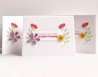May include: Three white textured greeting cards with floral decorations. Each card has a different flower: red, purple, and yellow. The phrase "THANK YOU FOR EVERYTHING" is printed on a banner across the centre of the cards.