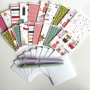 May include: A collection of colorful birthday cards with various patterns and illustrations, including reindeer, cakes, and balloons. Two pens, one lavender and one mint green, and several white envelopes are also present.