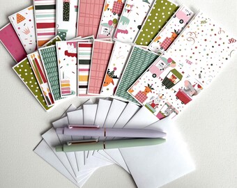 May include: A selection of birthday cards with diverse patterns and illustrations, such as reindeer, cakes, and balloons. Two pens, one lavender and one mint green, and several white envelopes are also present.