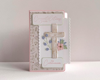 May include: A First Communion card featuring a wooden cross, floral details, and the phrases "Congratulations on your" and "First Communion." The card has a scalloped edge and a floral pattern on the left.