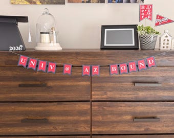 May include: A wooden chest of drawers with a banner reading "UNIV OF AZ BOUND" in red letters with a grey border. A black picture frame, a small potted plant, and graduation decorations are on top of the drawers.
