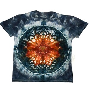 May include: A tie-dye t-shirt with a circular mandala design. The shirt features a dark blue and white background with a central orange and brown pattern. The short-sleeved shirt is made of soft fabric.