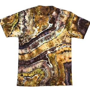 Pode incluir: Uma t-shirt de manga curta com um padrão tie-dye inspirado em geodos em tons de castanho, bege, verde-azeitona e roxo escuro. O design consiste em faixas orgânicas e onduladas de cor separadas por linhas brancas finas no tecido.