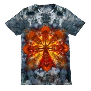 May include: A short-sleeved t-shirt with a tie-dye pattern. The shirt features a central design in shades of orange, red, and yellow, resembling a stylized flower or sun. The background is a blend of gray and blue hues.