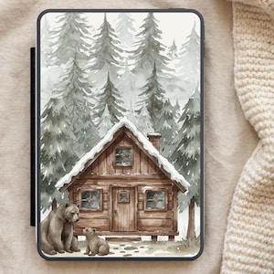 Puede incluir: Una funda para tableta con una ilustración en acuarela de una cabaña en un bosque nevado. Dos osos están sentados frente a la cabaña. La cabaña es marrón con un tejado cubierto de nieve, y el fondo es un bosque brumoso.