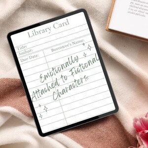 Puede incluir: Una tarjeta de biblioteca digital en una tableta con el texto "Emotionally Attached to Fictional Characters". La tarjeta tiene campos para título, autor, fecha de vencimiento y nombre del prestatario. La tableta está sobre una manta suave y texturizada con un libro y flores en el fondo.