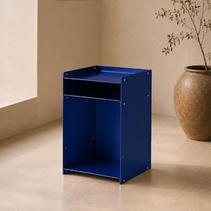May include: A cobalt blue metal side table featuring a rectangular top surface with raised edges, a single open storage shelf below, and a larger open compartment at the base. The structure is held together by visible silver-toned metal screws.