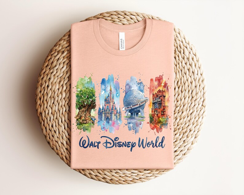 May include: A peach-colored t-shirt featuring a watercolor design of Walt Disney World landmarks. The design includes the Tree of Life, Cinderella Castle, Spaceship Earth, and the Tower of Terror, with the words "Walt Disney World" in navy blue.