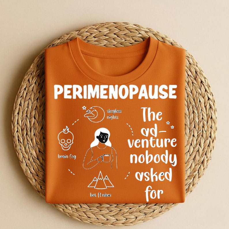 Puede incluir: Una camiseta naranja con la palabra "PERIMENOPAUSE" en blanco. La camiseta presenta un gr&aacute;fico con el texto "The ad-venture nobody asked for" e ilustraciones de niebla mental, noches de insomnio y sofocos.