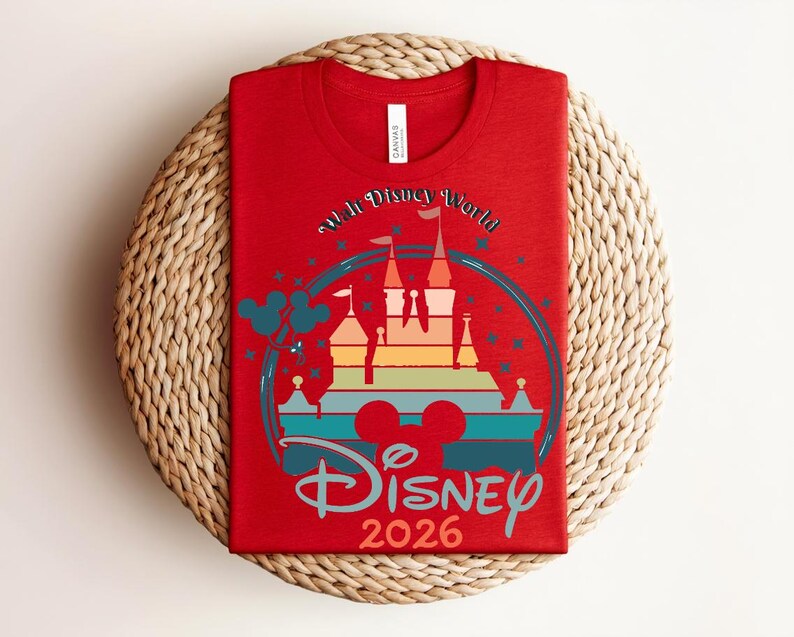 Op de afbeelding: Een rood t-shirt met een kleurrijke afbeelding van een kasteel, de tekst "Walt Disney World" en "Disney 2026". Het ontwerp bevat Mickey Mouse oren en een regenboogkleurige kasteelsilhouet. Voor Disney-liefhebbers.