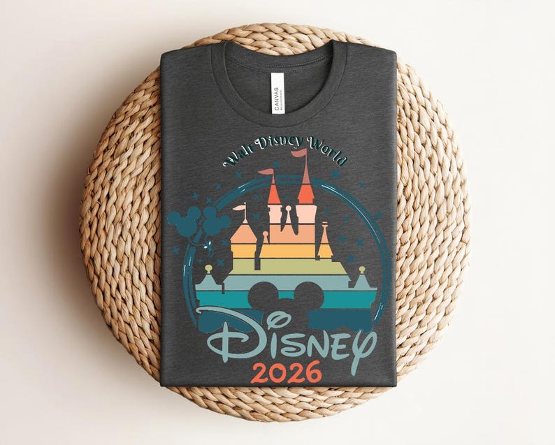 Op de afbeelding: Donkergrijs t-shirt met een kleurrijke afbeelding van een kasteel, de tekst "Walt Disney World" en "Disney 2026". Het ontwerp bevat een regenboog kasteel silhouet en Mickey Mouse oren.