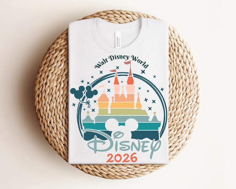 Op de afbeelding: Wit T-shirt met een kleurrijke afbeelding van een kasteel, Mickey Mouse oren en de tekst "Walt Disney World" en "Disney 2026". Het ontwerp heeft een regenboog aan kleuren en sterren, met een blauwe omtrek.