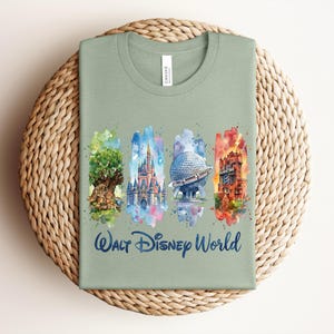 May include: Sage green t-shirt featuring watercolor illustrations of iconic Walt Disney World landmarks. The design includes the Tree of Life, Cinderella Castle, Spaceship Earth, and the Tower of Terror, with "Walt Disney World" written below.