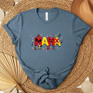 May include: A blue t-shirt with the word "MAMA" in red and yellow, featuring cartoon characters and hearts. The shirt is made of soft material and has short sleeves.