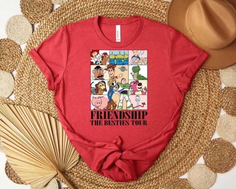May include: Red t-shirt featuring a colorful graphic of cartoon characters in a grid, with the words "FRIENDSHIP THE BESTIES TOUR" in a bold font. The shirt is made of a soft material and has a classic crew neck design.