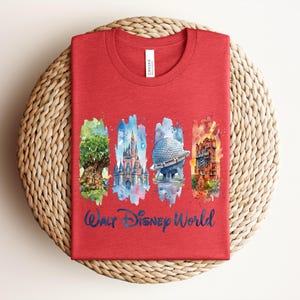 May include: Red t-shirt featuring watercolor illustrations of iconic Walt Disney World landmarks: the Tree of Life, Cinderella Castle, Spaceship Earth, and the Tower of Terror. The words "Walt Disney World" are written in blue script below the images.