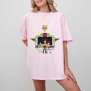 K&ouml;nnte beinhalten: Hellrosa T-Shirt mit einem Aufdruck aus dem Film Toy Story 5. Der Aufdruck zeigt den Filmtitel, die Zahl 5 und die Charaktere Woody, Buzz Lightyear und Jessie. Das T-Shirt hat kurze &Auml;rmel und einen Rundhalsausschnitt.