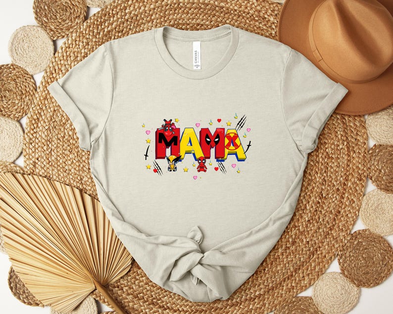 May include: A light beige t-shirt with the word "MAMA" in red and yellow block letters, decorated with cartoon characters and hearts. The shirt is made of a soft material and has short sleeves.