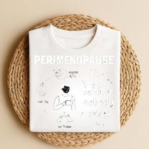 Puede incluir: Camiseta blanca de cuello redondo con la palabra "PERIMENOPAUSE" en letras grandes y en negrita. La camiseta presenta una ilustraci&oacute;n en blanco y negro con texto, incluyendo "The ad-venture nobody asked for."