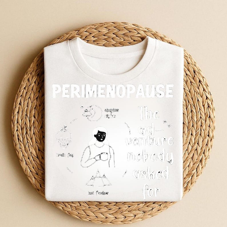 Puede incluir: Camiseta blanca de cuello redondo con la palabra "PERIMENOPAUSE" en letras grandes y en negrita. La camiseta presenta una ilustraci&oacute;n en blanco y negro con texto, incluyendo "The ad-venture nobody asked for."
