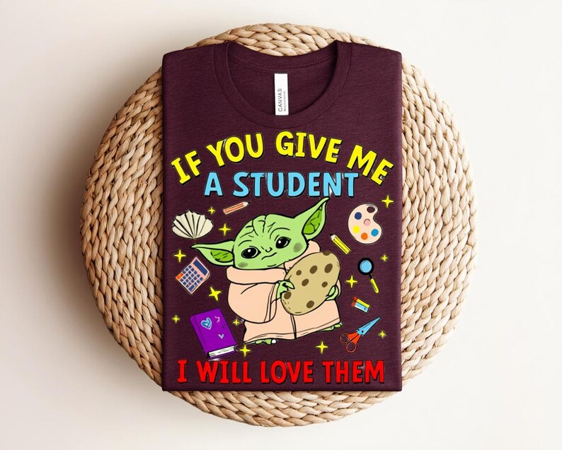May include: Burgundy t-shirt with a graphic of a green alien-like character holding a cookie, surrounded by school supplies. Text reads "IF YOU GIVE ME A STUDENT I WILL LOVE THEM" in yellow and red.