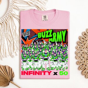 Puede incluir: Una camiseta rosa claro con un gr&aacute;fico de Buzz Lightyear y el texto "BUZZ ARMY" en verde y naranja. El gr&aacute;fico incluye m&uacute;ltiples figuras de Buzz Lightyear. El texto "INFINITY x 50" tambi&eacute;n se muestra en rosa y verde.