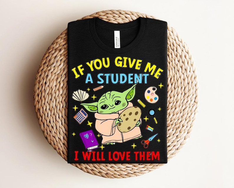 May include: Black t-shirt with a graphic of a green alien-like character holding a cookie, surrounded by school supplies. Text reads "IF YOU GIVE ME A STUDENT I WILL LOVE THEM" in yellow and red.