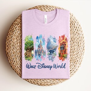 May include: A light purple t-shirt featuring watercolor illustrations of iconic Walt Disney World landmarks. The shirt includes images of the Tree of Life, Cinderella Castle, Spaceship Earth, and Tower of Terror, with the words "Walt Disney World" in script.