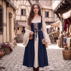 May include: A woman wearing a medieval-style dress with a cream-colored bodice and sleeves, and a dark blue skirt. The dress features a laced bodice and a brown belt. She is holding a small brown pouch and a rolled-up item. The background shows a cobblestone street and old buildings.
