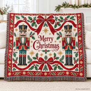 May include: A woven throw blanket featuring a cream background with two nutcracker figures in red, blue, and gold uniforms. The design includes red ribbons, green holly leaves, red berries, and gold stars with the text Merry Christmas.