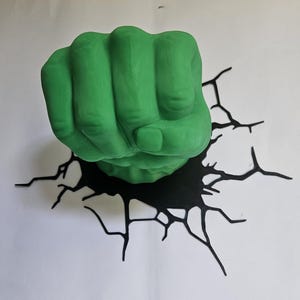 Könnte beinhalten: Ein grüner, geballter Faust, die aus einer schwarzen, zerbrochenen Oberfläche hervortritt. Die Faust ist leuchtend grün, und die Risse sind schwarz, wodurch ein 3D-Effekt entsteht. Das Kunstwerk befindet sich vor einem weißen Hintergrund.