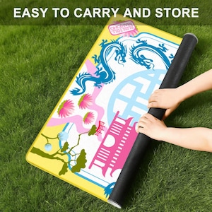 May include: A colorful mat with a dragon design is rolled up, held by hands. The mat features a yellow border, a blue dragon, pink flowers, and the text "EASY TO CARRY AND STORE". The mat is on a green grassy surface.