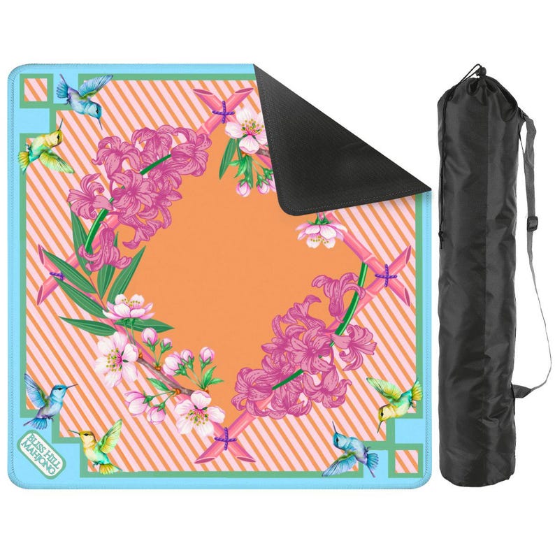 May include: A square game mat with a light blue border and an orange striped center featuring pink hyacinth flowers, cherry blossoms, and hummingbirds. The text "BLISS HILL MAHJONG" is printed in the corner. Includes a black carrying bag.