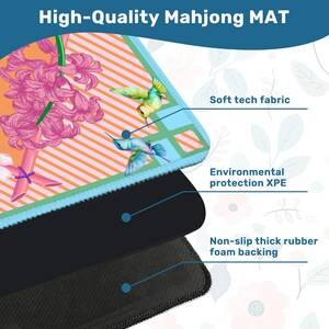 May include: A rectangular Mahjong mat featuring a vibrant orange and light blue striped pattern with pink hyacinth flowers and two hummingbirds. The mat displays three layers: a soft tech fabric top, an XPE middle, and a non-slip rubber foam backing.